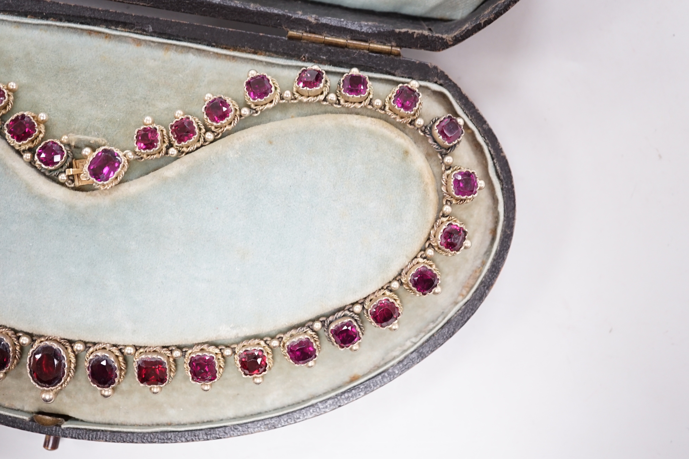 A cased 19th century gilt white metal and graduated oval and square cut garnet set fringe necklace, lacking drop, 37cm.